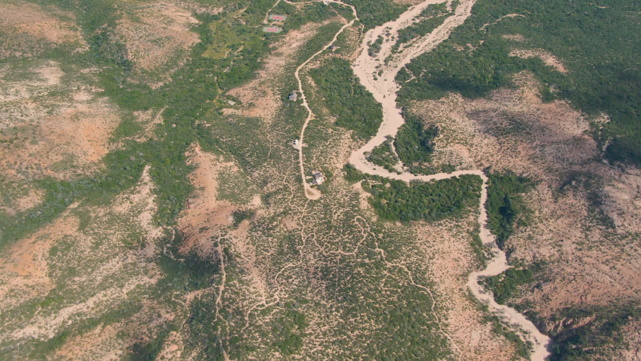 Aerial frame from Cabo Pulmo, Baja California Sur, Mexico, showing a pale riverbed curving through dry green and tan scrubland with no visible people.