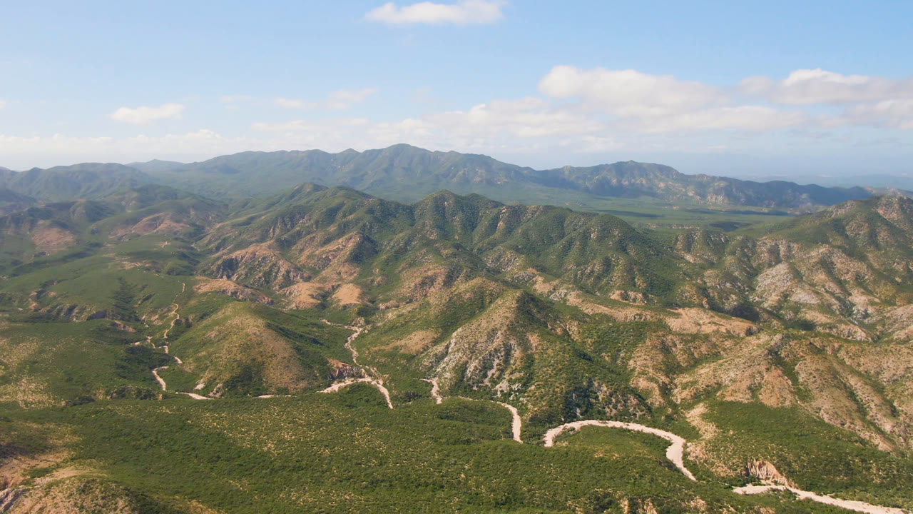 Drone-height landscape of mountains, valleys, and scattered clouds.