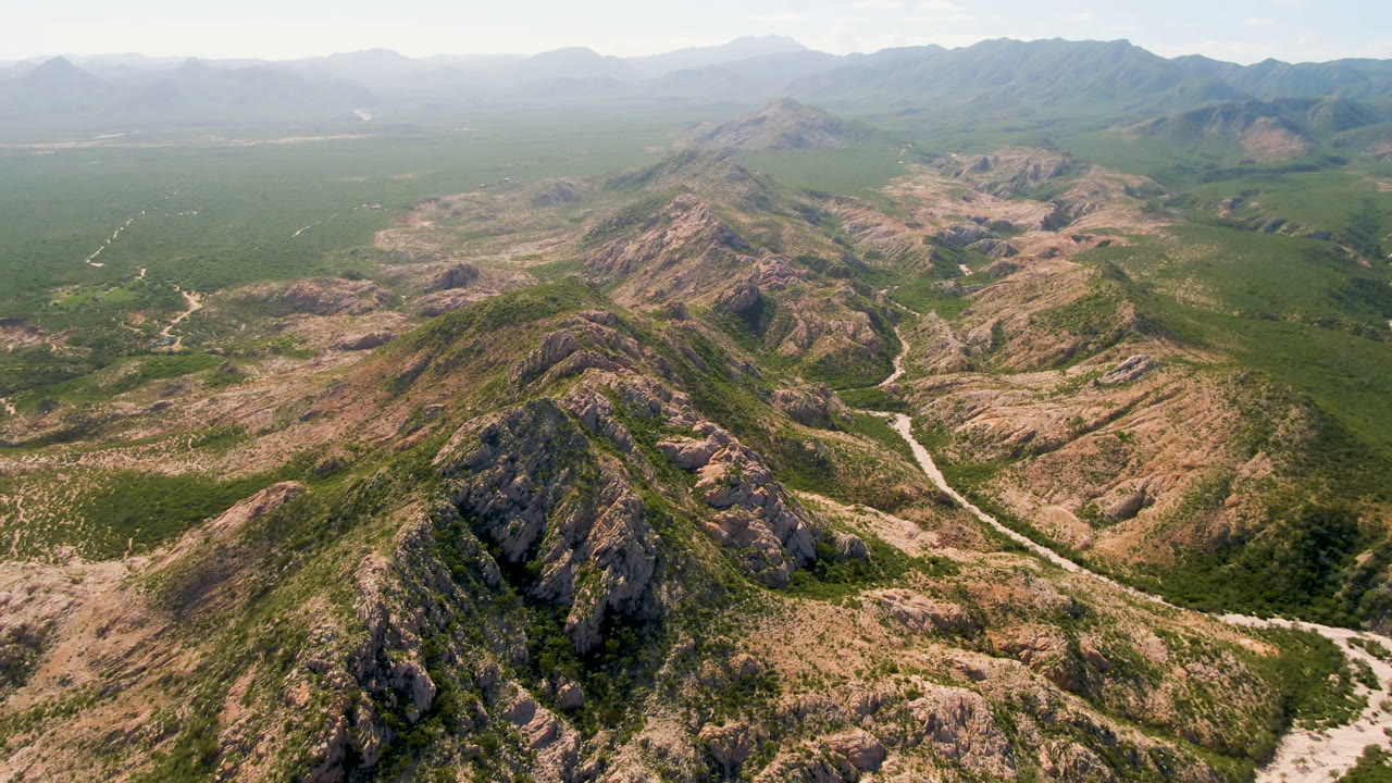 Aerial frame over rugged Cabo Pulmo mountain ridges, with pale winding tracks crossing scrub-covered valleys and no visible people.