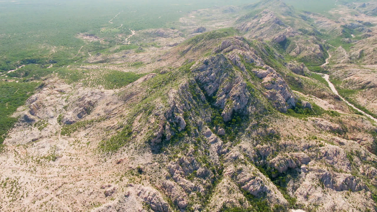Aerial frame looking along the central rocky ridge in Cabo Pulmo, with pale stone, green vegetation, a narrow valley route, and no visible people.