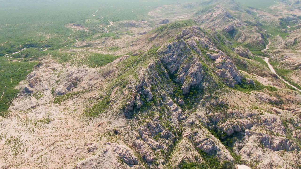 Drone view of rugged mountain ridges above a dry green valley.