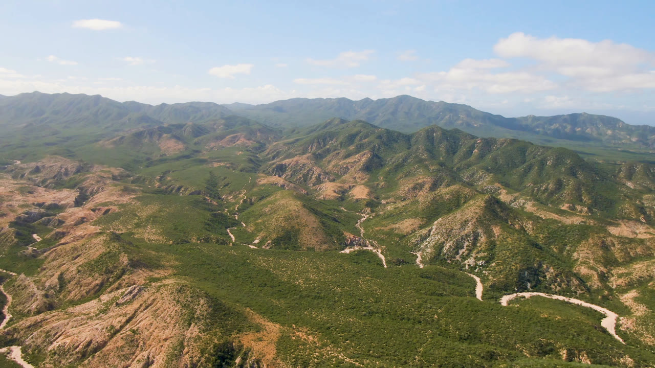 Drone-like view across rugged hills with dirt tracks and distant mountains.