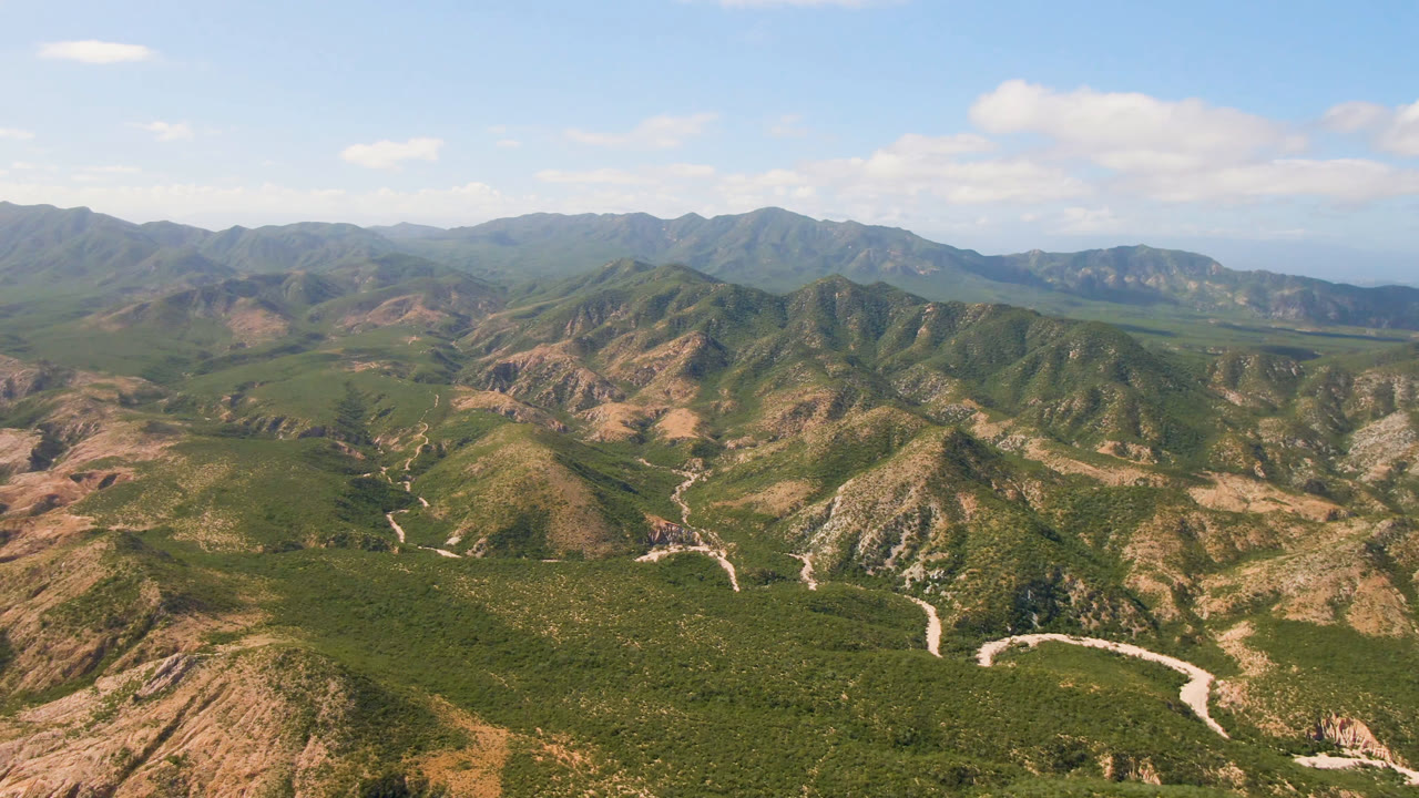 Aerial mountain scene with branching dirt roads and distant coastline on the horizon.
