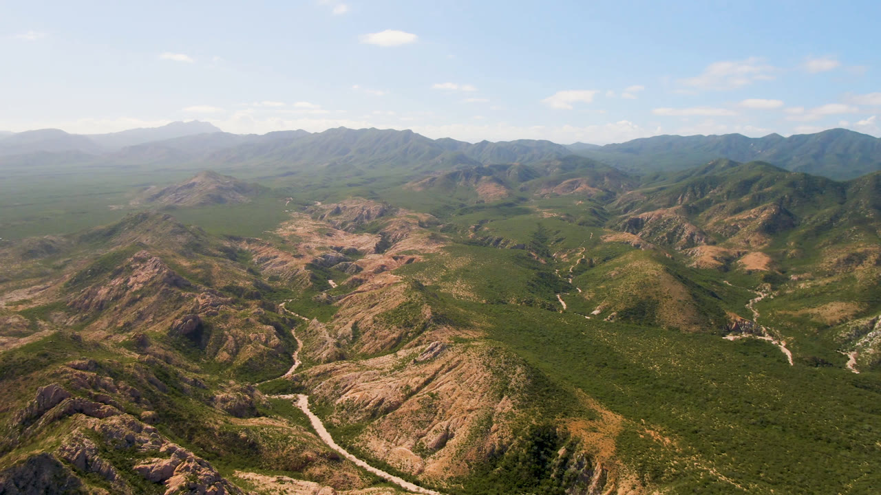 Aerial panorama of rugged mountains with a road threading through dry green terrain.
