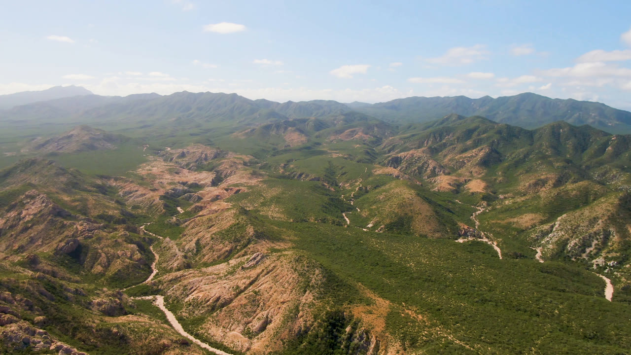 Wide aerial landscape with desert mountains, green valley cover, and a winding road