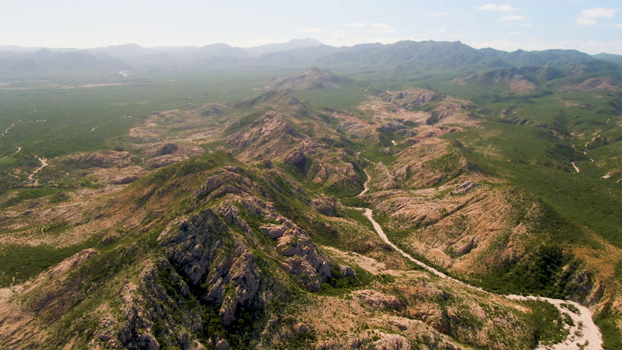 Drone-height landscape of mountain ridges, scrub, and a winding track