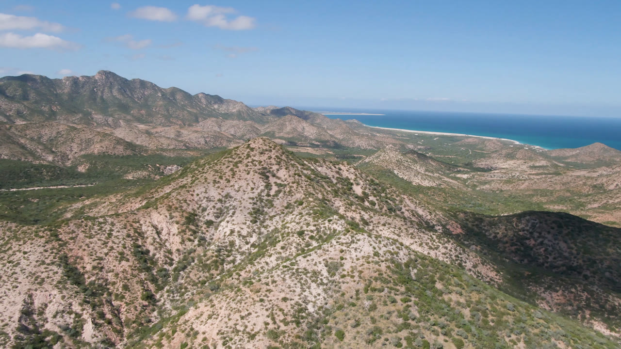 Opening frame of Cabo Pulmo, Baja California Sur, with a scrubby mountain ridge in the foreground, rocky hills behind it, blue ocean on the horizon, and no visible people.