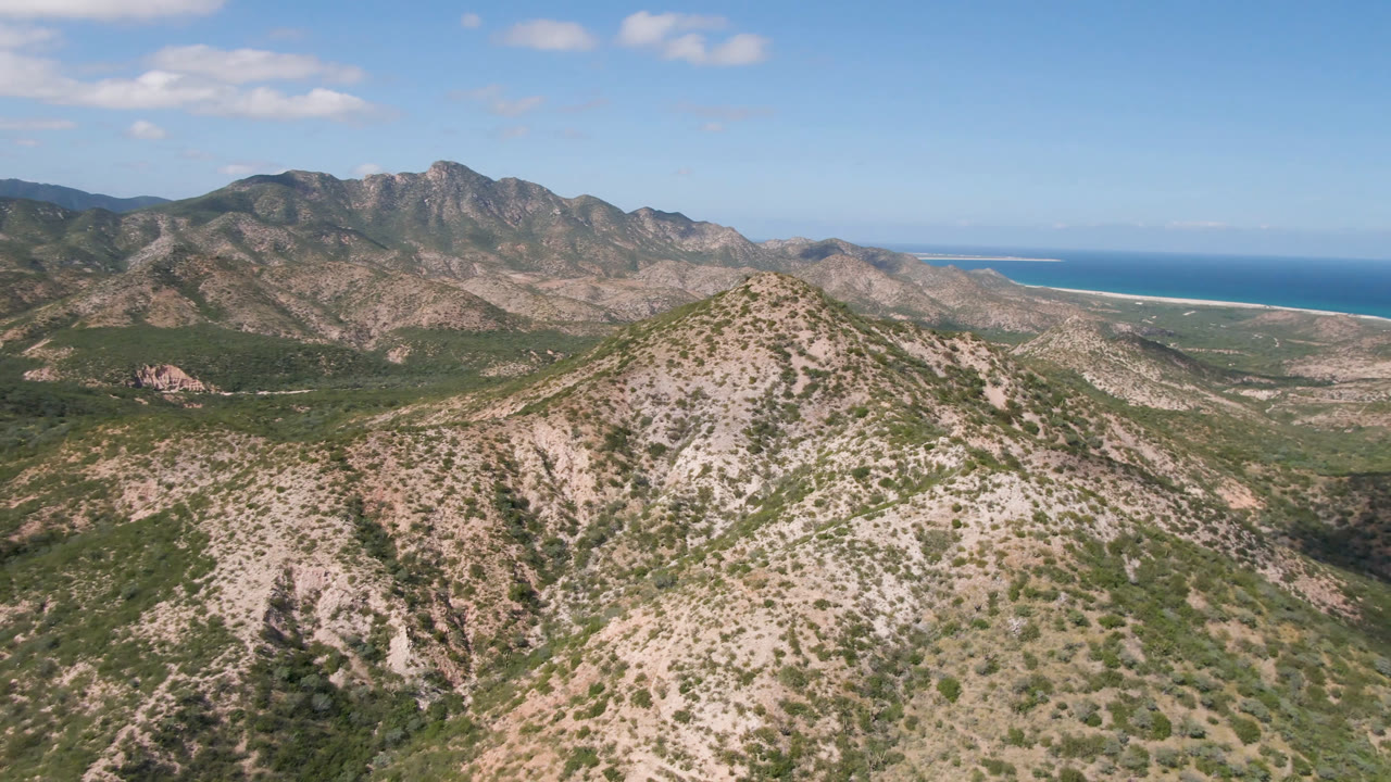 Aerial view in Cabo Pulmo, Baja California Sur, centered on the foreground ridge, with darker mountain slopes behind it, ocean at right, and no visible people.
