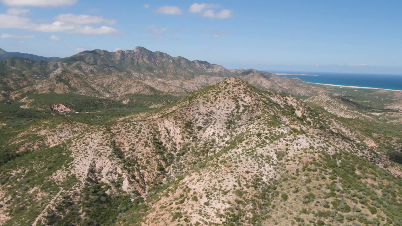 Wide aerial landscape of scrubby mountains with a blue ocean horizon.