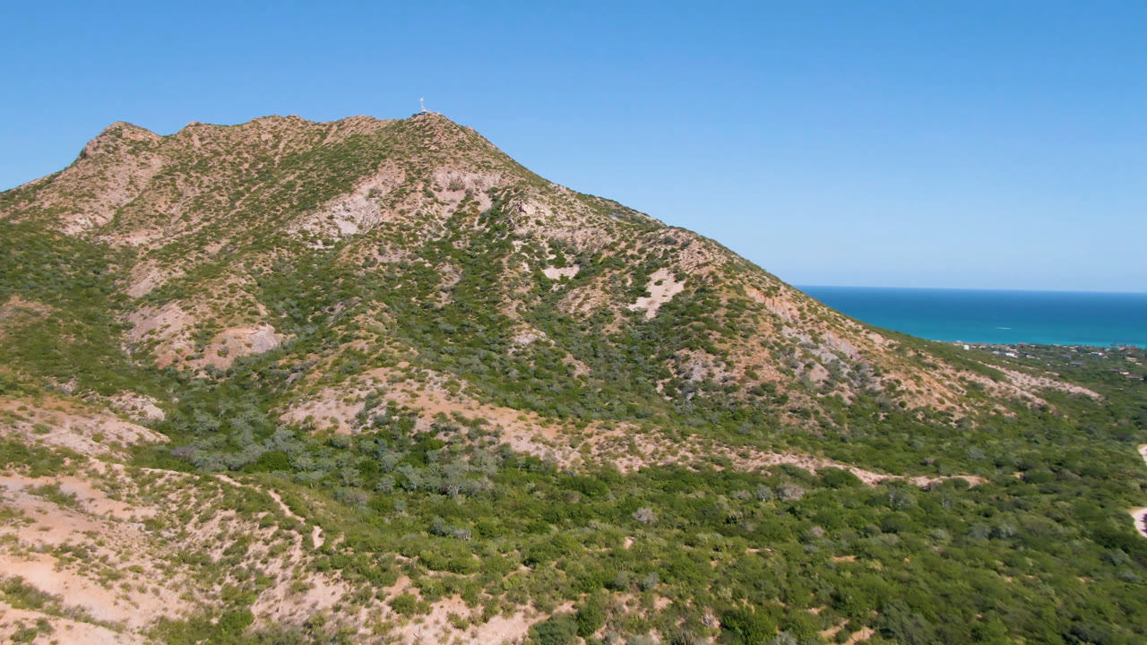 Rocky desert mountain with ocean horizon under clear blue sky.