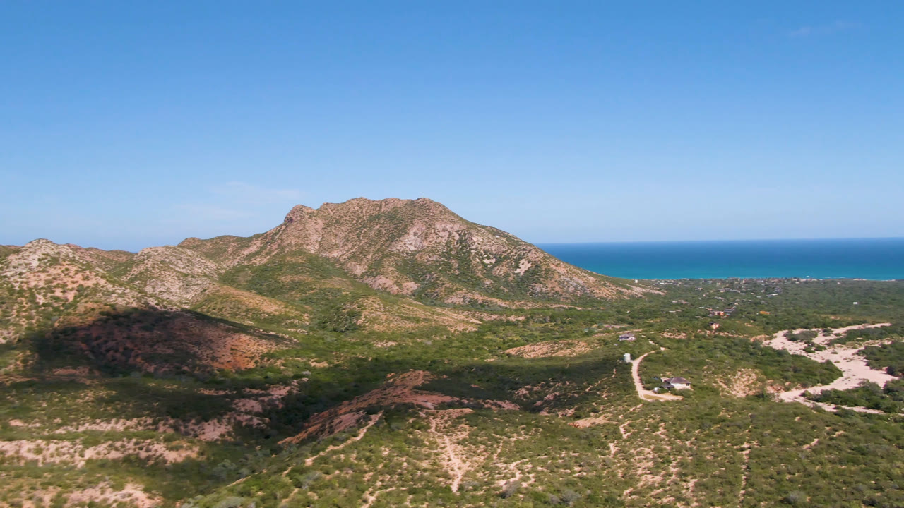 Aerial view of rocky hills, dirt roads, and ocean horizon under blue sky.