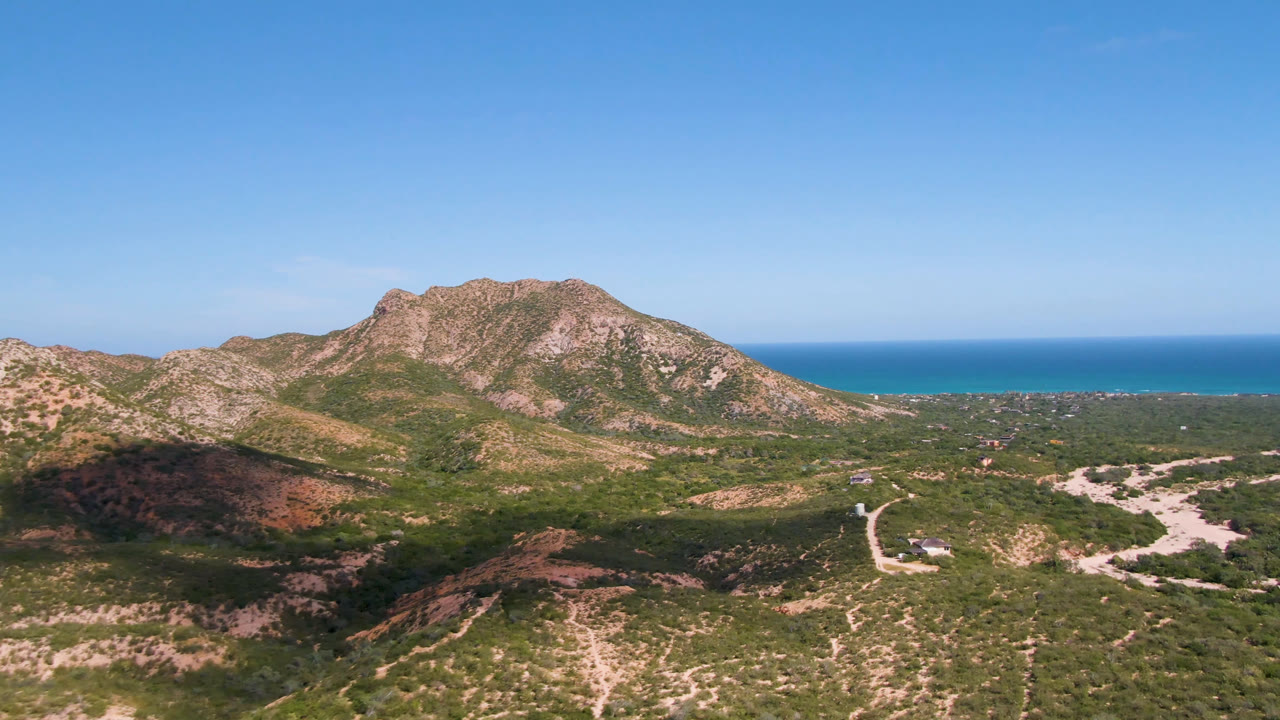 One second into the Cabo Pulmo aerial, the rocky ridge fills the center with dirt roads below, ocean beyond, and no visible people.