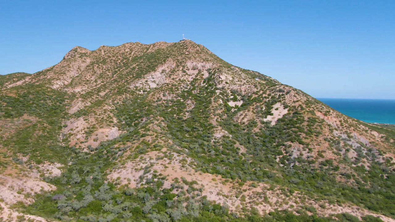 Opening frame of a rocky scrub-covered mountain ridge in Cabo Pulmo, Baja California Sur, with a blue ocean strip behind the slope and no visible people.