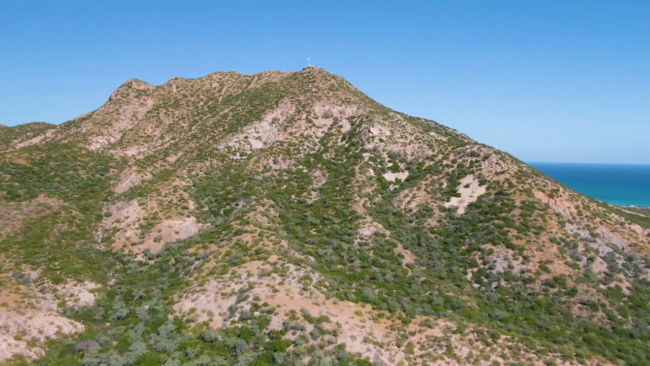Second frame shows the Cabo Pulmo mountain peak centered higher in the shot, with sparse vegetation, exposed rock, blue sky, and no visible people.