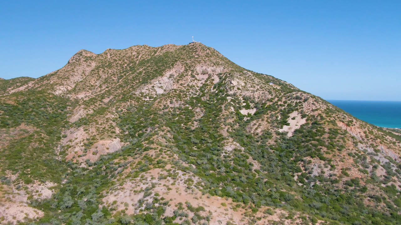 Mountain slope with patches of rock, shrubs, blue sky, and ocean horizon