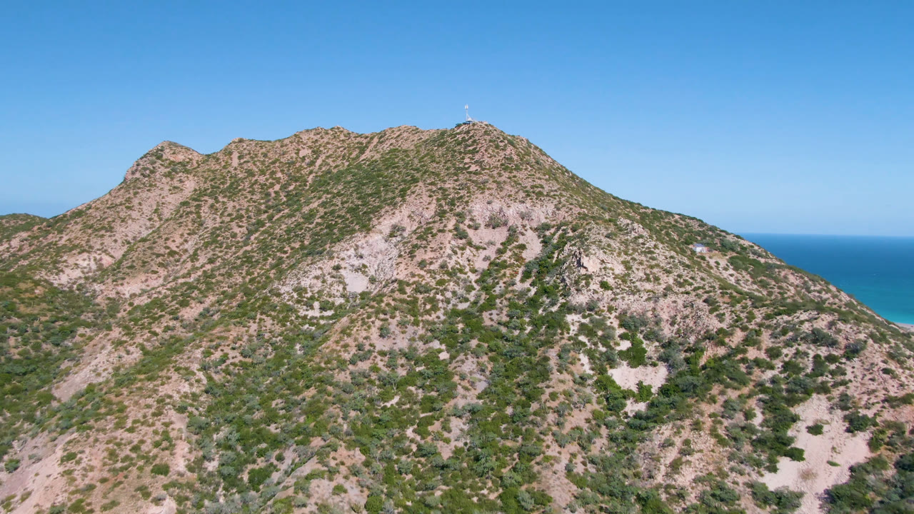 Opening frame of a rugged mountain ridge in Cabo Pulmo, Baja California Sur, with blue ocean visible behind the slope and no visible people.