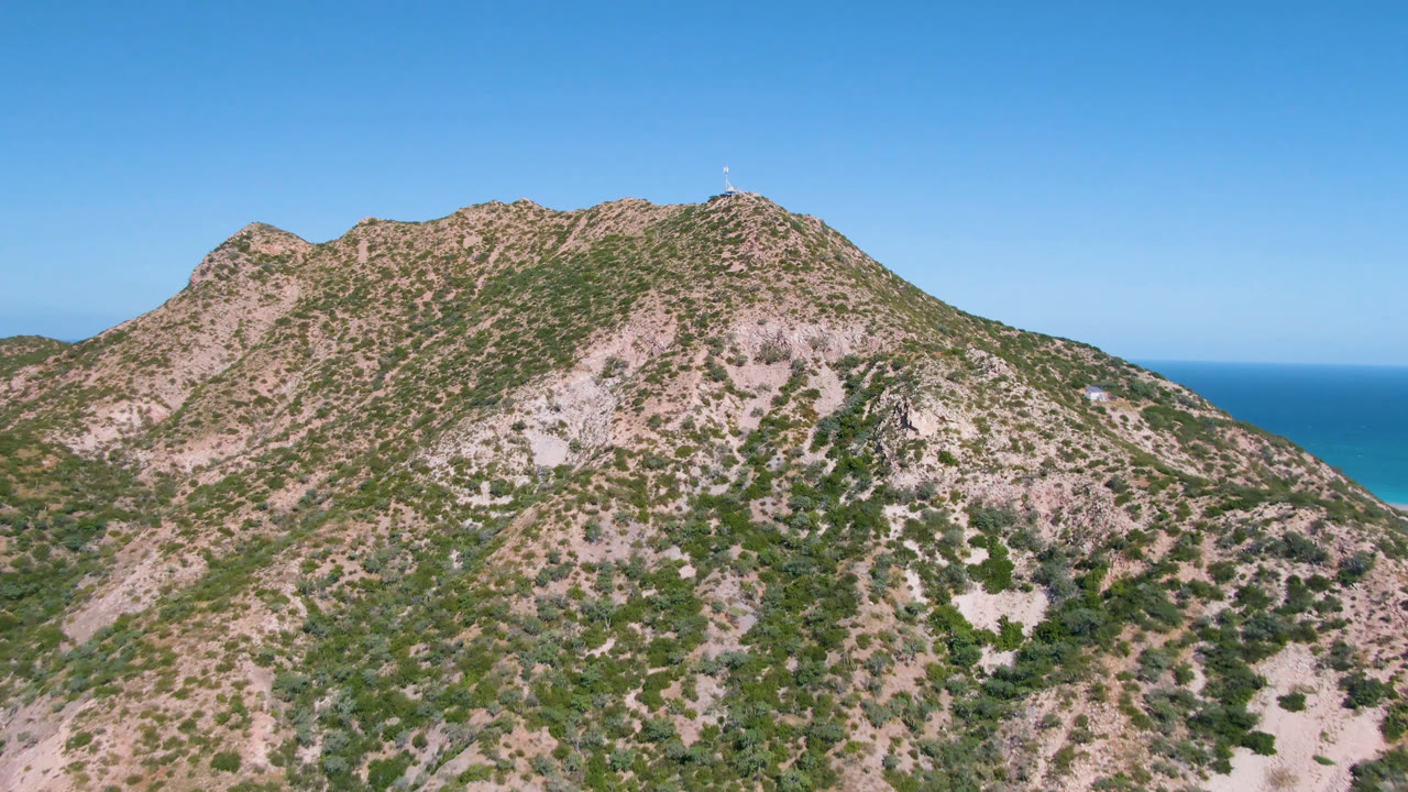 Second frame shows the Cabo Pulmo mountain ridge slightly farther across the slope, with patchy vegetation, exposed rock, blue ocean, and no visible people.