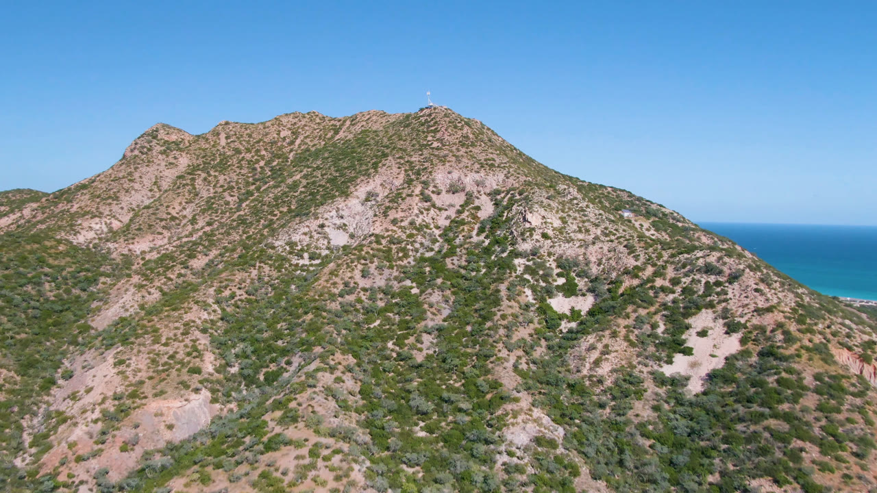 Mountain slope with scattered vegetation and a blue sea background