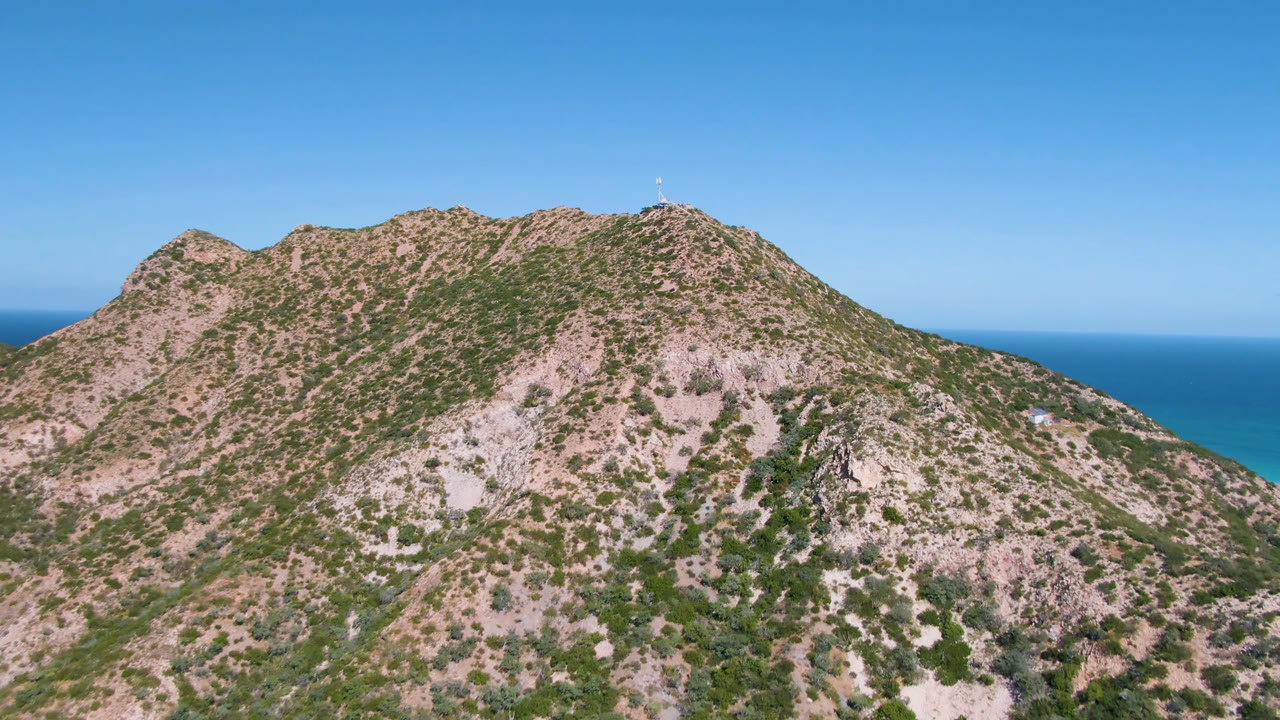 Aerial view in Cabo Pulmo, Baja California Sur, showing a rocky shrub-covered mountain ridge with deep blue ocean on the left horizon and no visible people.