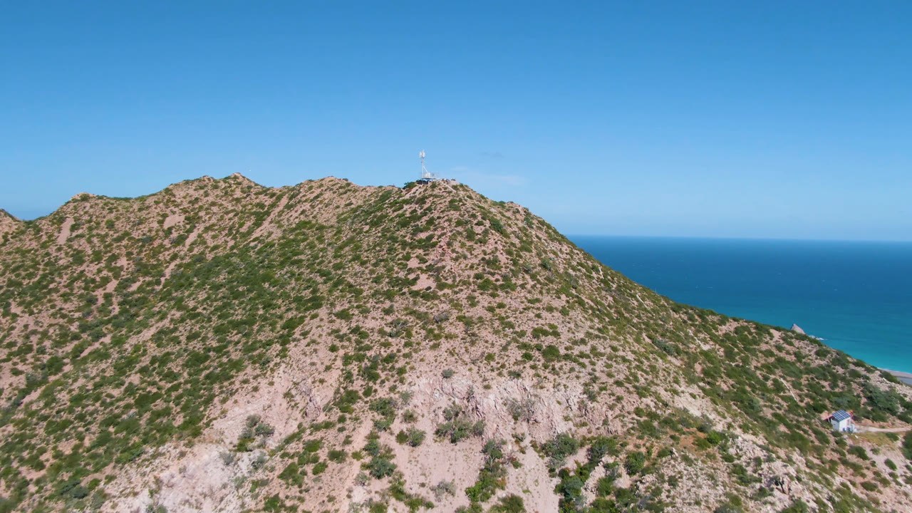Rocky scrub mountain above blue ocean under clear sky