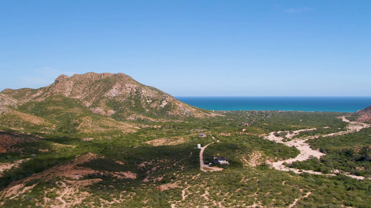 Aerial landscape with rugged hills, coastal plain, and blue sea.