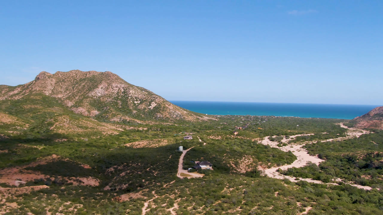 Aerial view of scrubland roads, rocky mountain, and ocean horizon