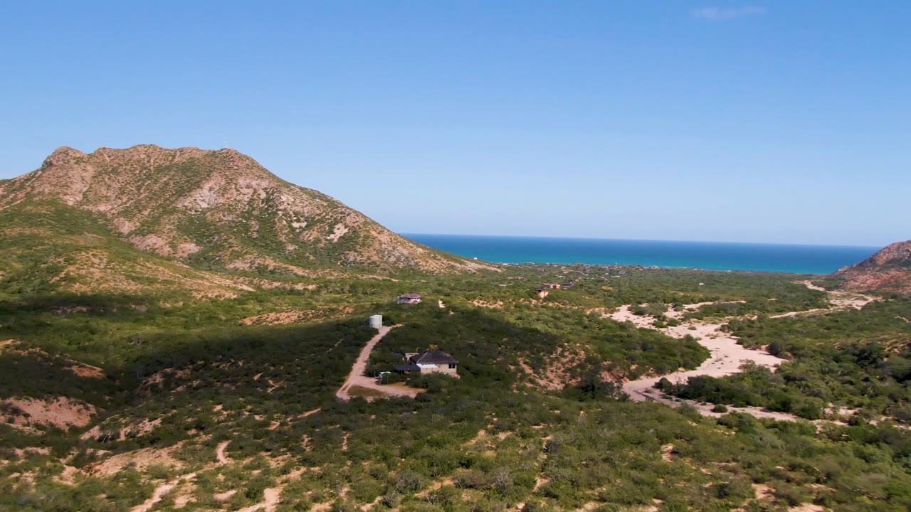 Desert hills with a house, dirt roads, mountains, and ocean horizon