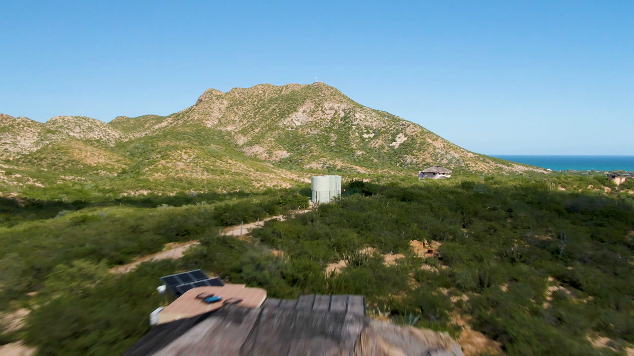 At 0:01, the Cabo Pulmo aerial view centers scrubby field and a pale cylindrical water tank below rocky hills, with the ocean line visible and no visible people.