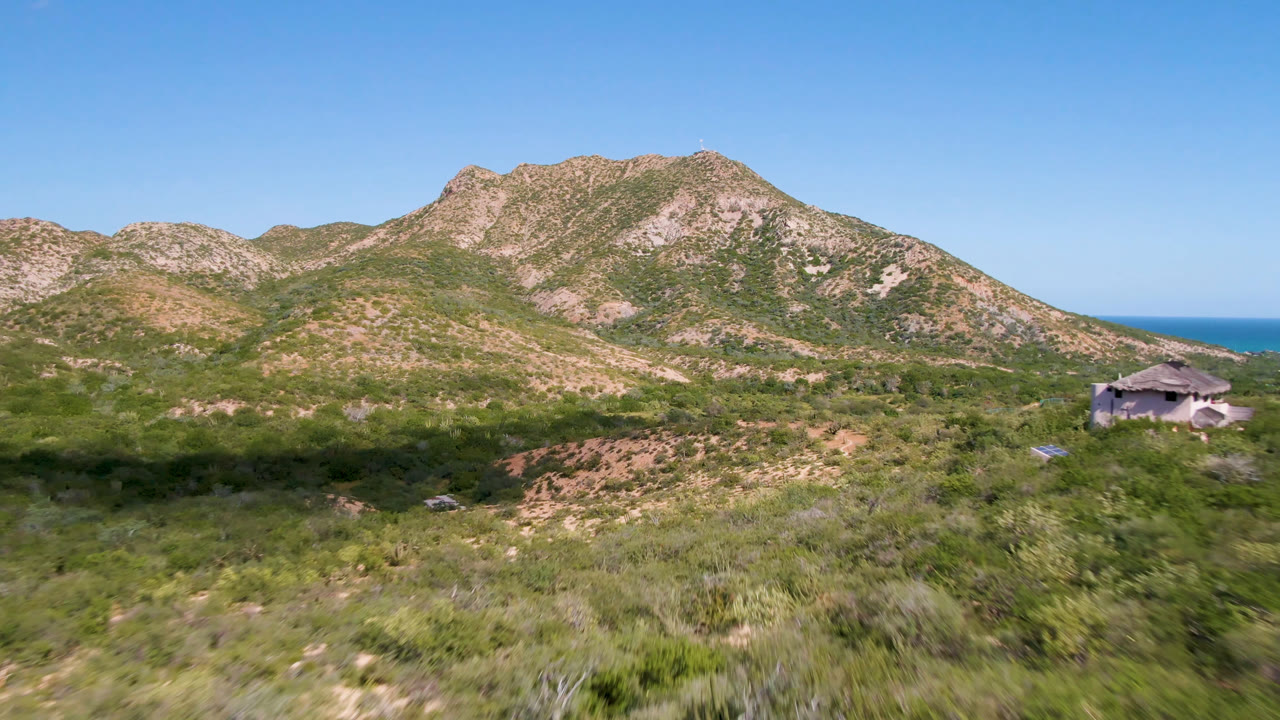 Rocky hills and scrubland with ocean horizon and a structure near the right edge.