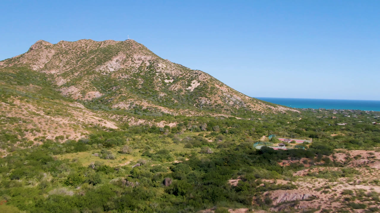 Rocky hills above green scrubland with ocean on the horizon.