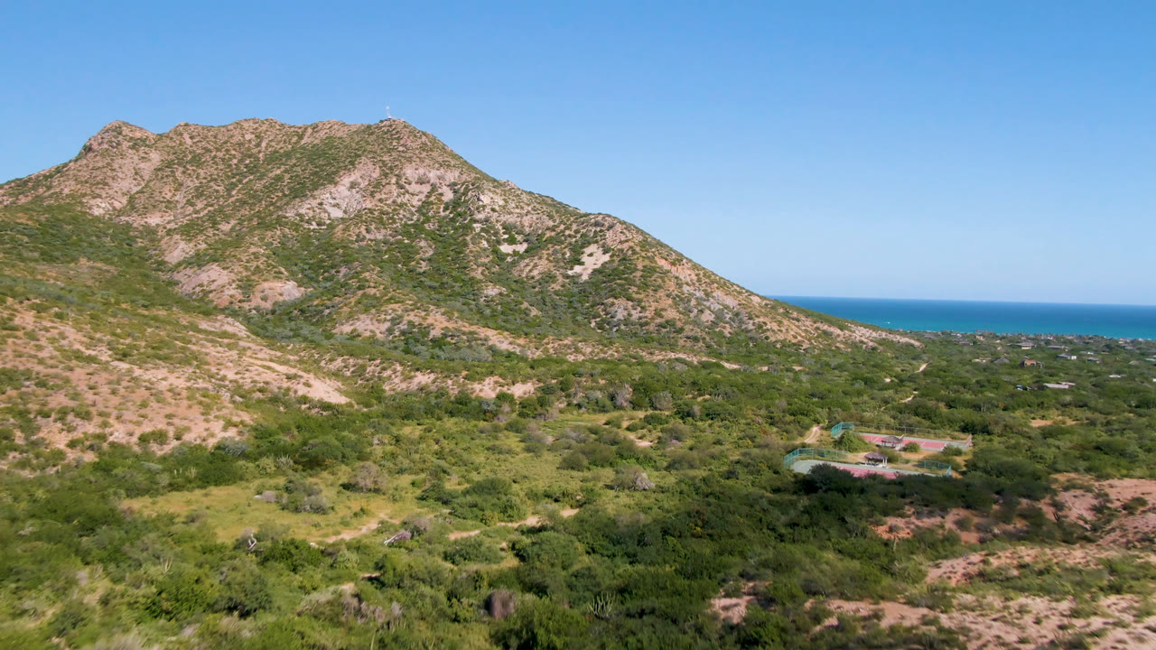 Cabo Pulmo aerial frame with the mountain centered, low vegetation across the foreground, ocean visible behind the hillside, and no visible people.