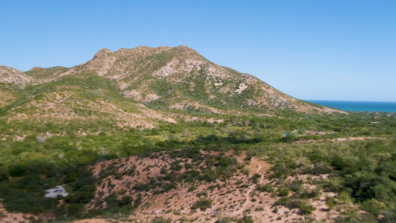 Opening frame of Cabo Pulmo, Baja California Sur, showing rocky green-tan mountains, desert brush in the foreground, a thin blue ocean horizon, and no visible people.