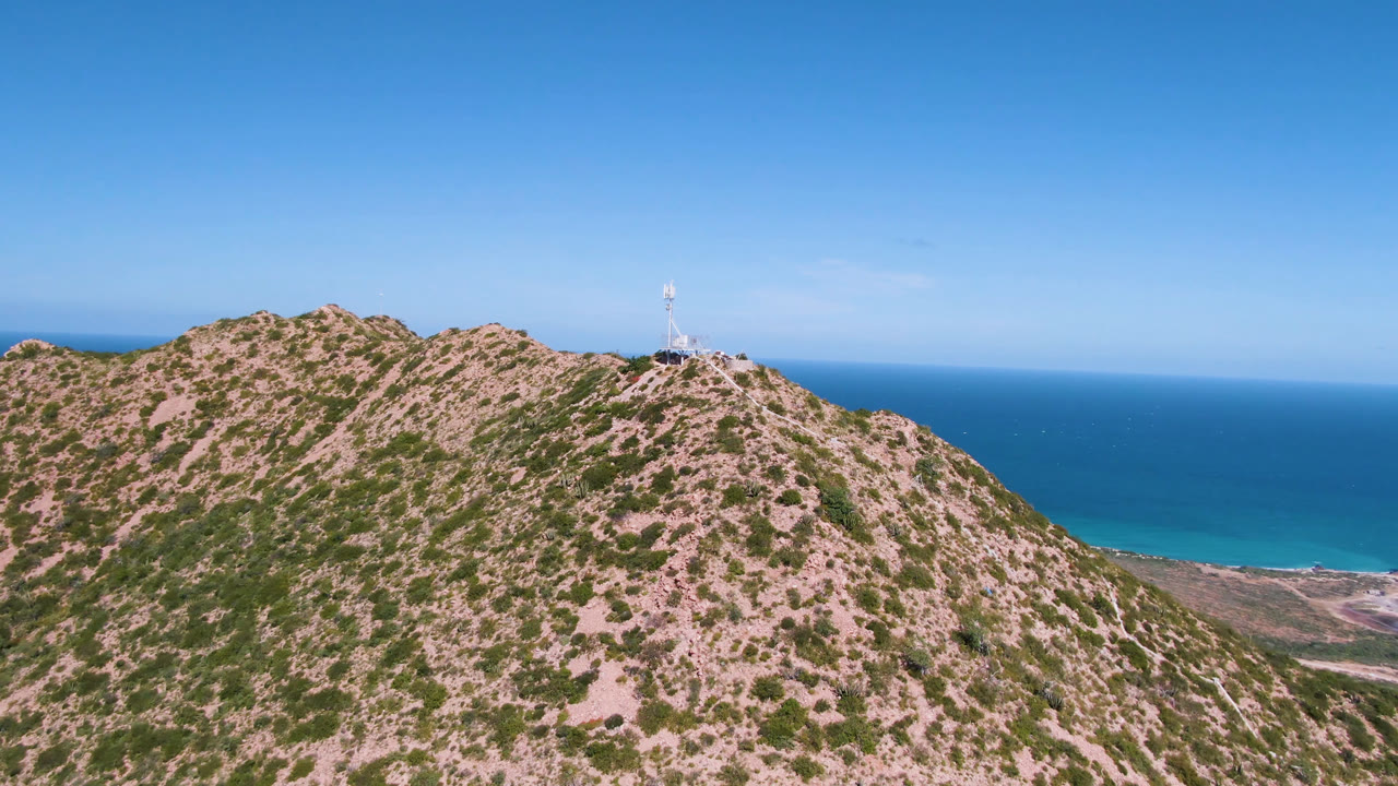 Rocky hilltop with a small lighthouse and blue ocean beyond.