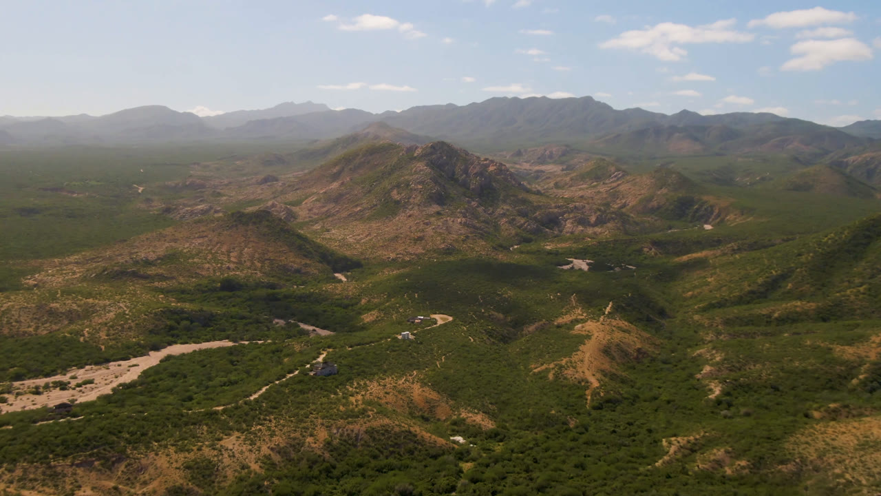 High aerial view across arid hills, green vegetation, and layered mountain ranges.