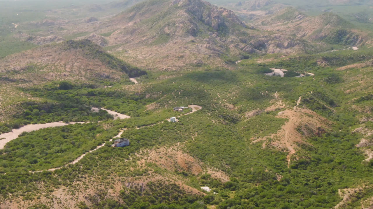 High aerial view of mountain ridges, scrubland, a winding track, and a dry wash.