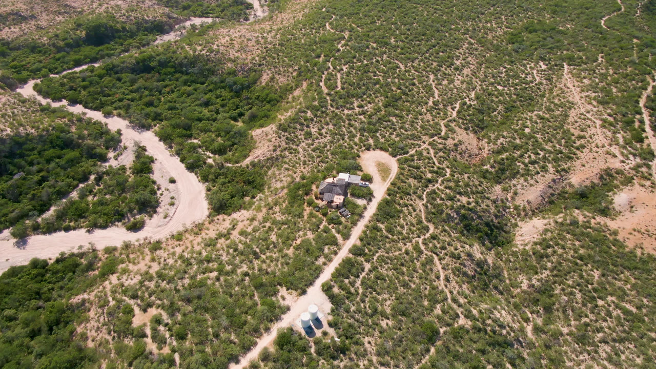 Overhead view of scrubland, dirt road, and a small rural house compound.