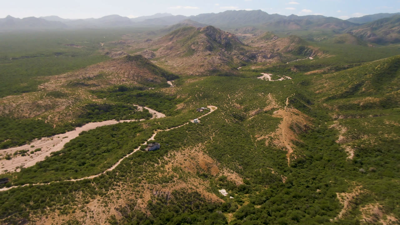 Aerial view of a winding dirt road through green desert hills and mountains.