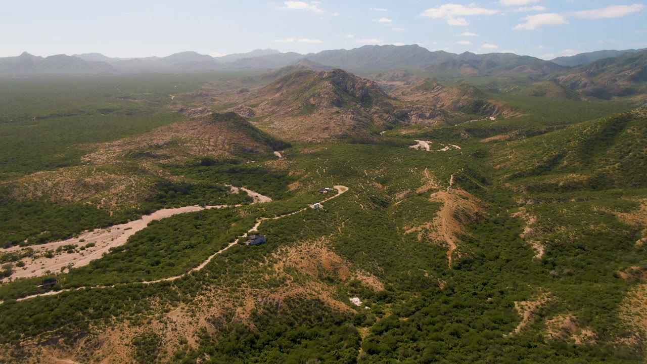 Drone view across rugged green hills, a winding road, and a hazy mountain horizon.
