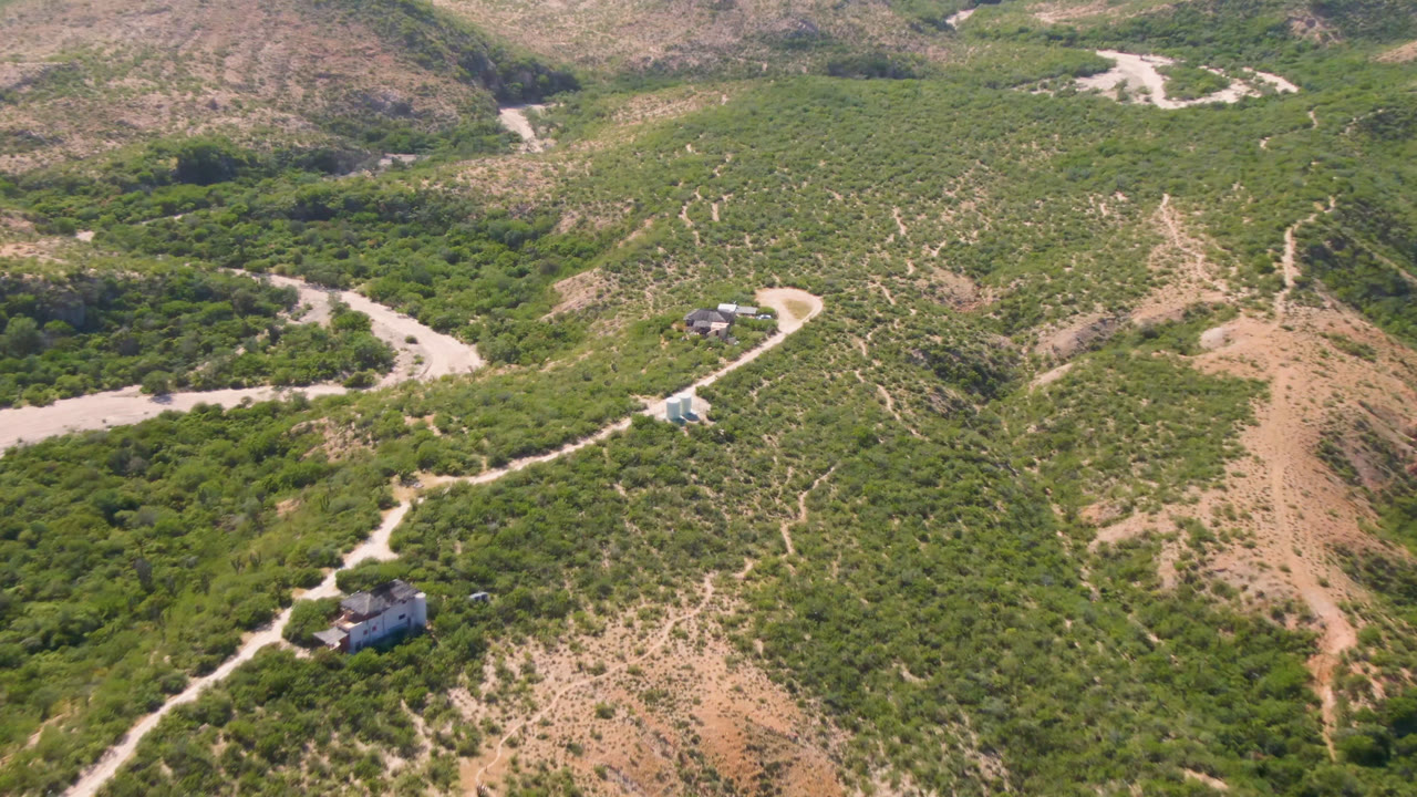 Aerial view of a winding dirt road through green desert hills.