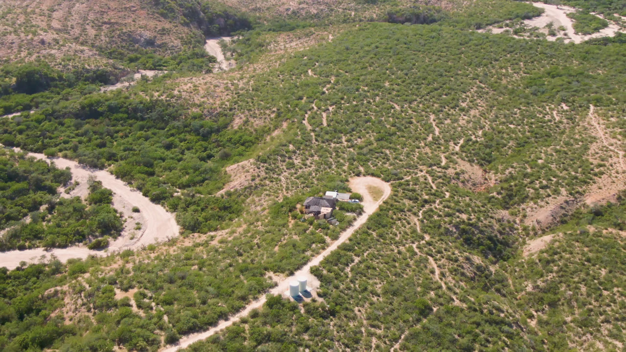 Aerial view of a winding pale road through scrub-covered hills.