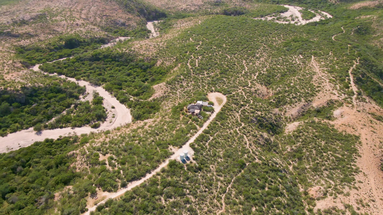 Aerial view of a winding dirt road through green scrub and tan hills