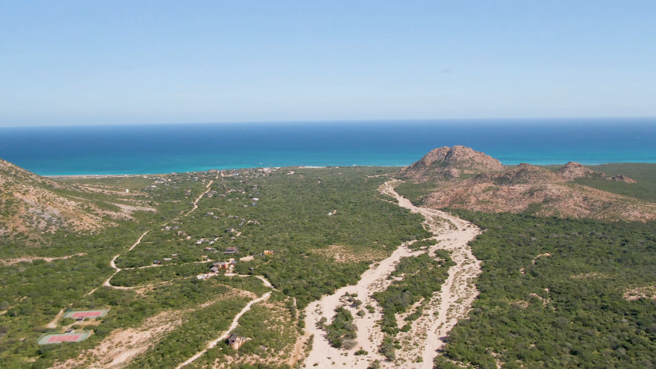 Aerial view of dirt roads, green scrub, rocky hills, and blue ocean.