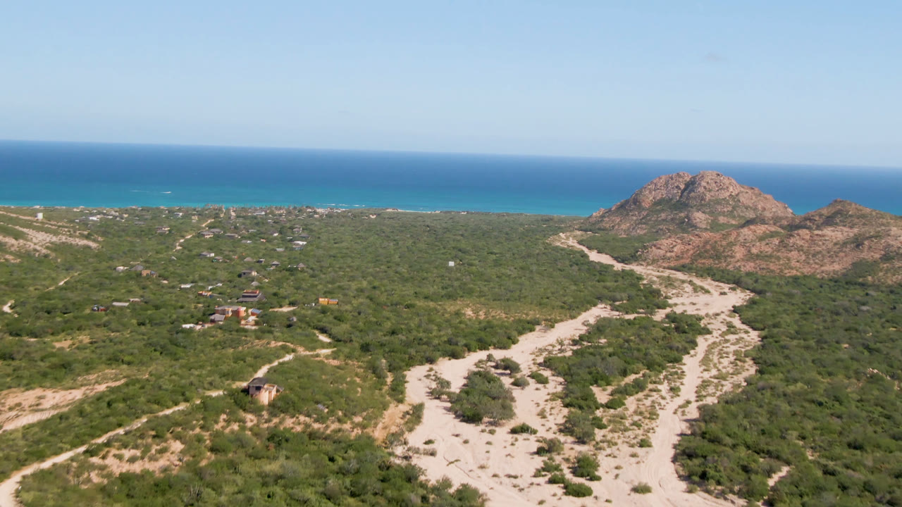 Aerial view of winding dirt roads, scrubland, rocky hills, and ocean horizon.