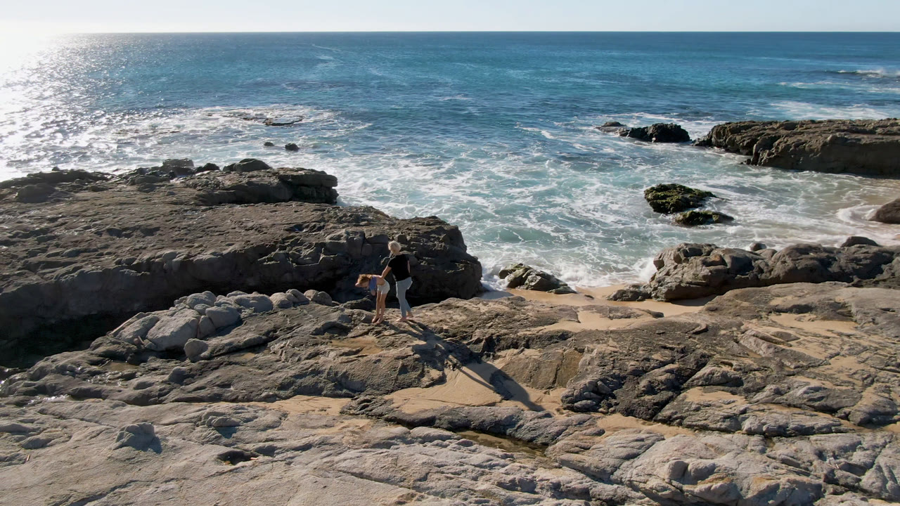 Two people standing on rocks above surf and tide pools.