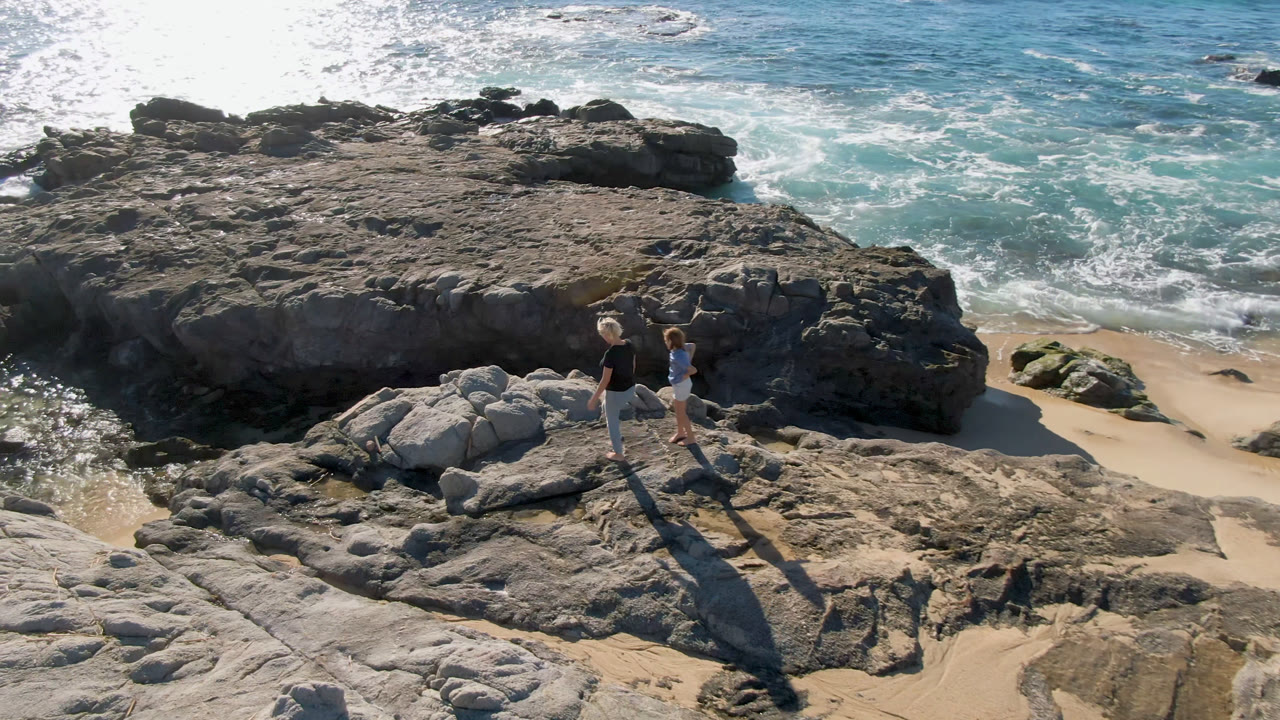 Two people moving across rocks beside a small sandy beach.
