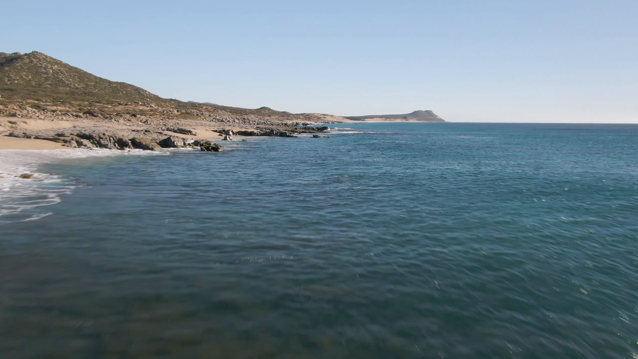 Aerial view of blue ocean beside a rocky sandy coast under clear sky