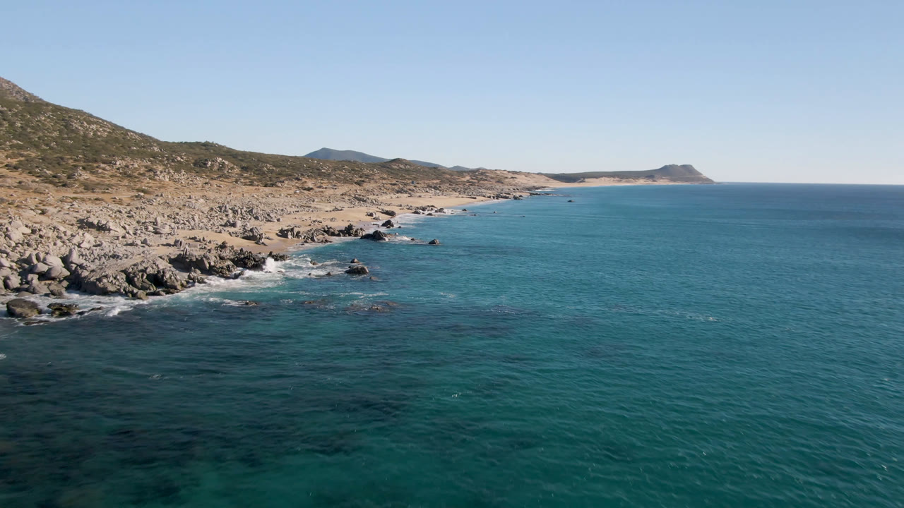 Wide aerial coastline with rocky beach, blue ocean, and distant headland