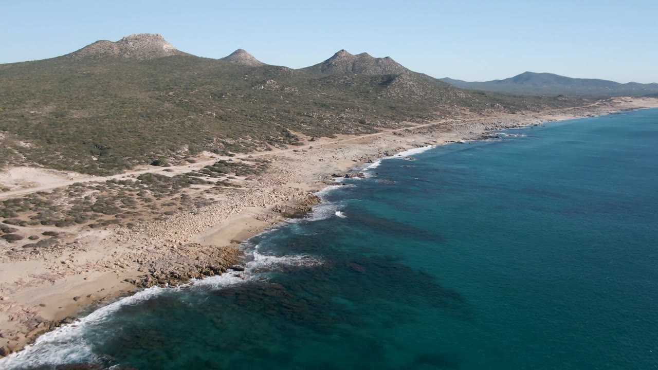Wide aerial of beach curve, open water, and mountain ridge