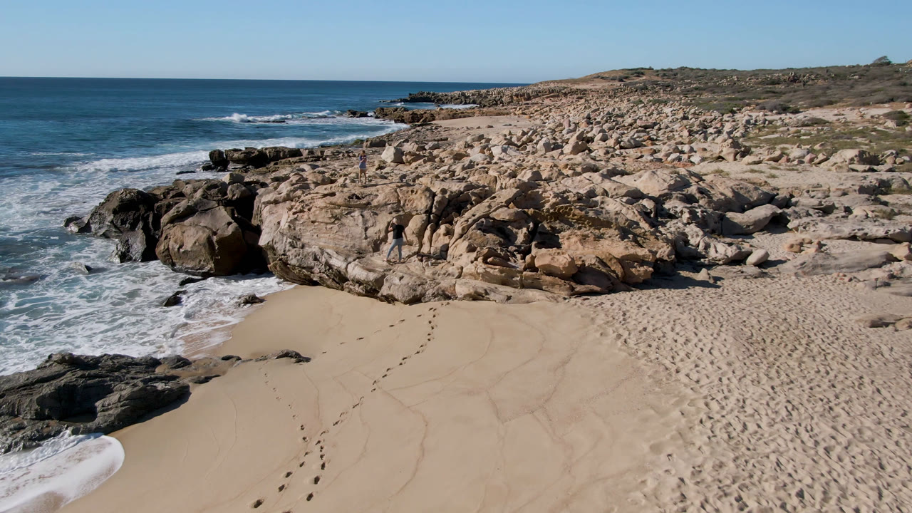Rocky beach cove with footprints in sand and ocean surf on the left.
