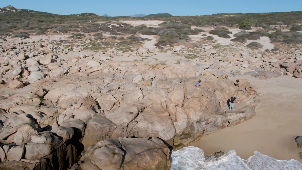 High-angle coastal rocks with surf entering at the lower right and small people on the formations.